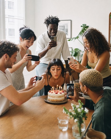 Friends around a birthday cake, filming the moment on their phones